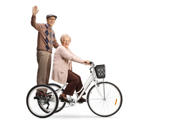 Wall Mural - Senior man waving from a tricycle and senior woman riding