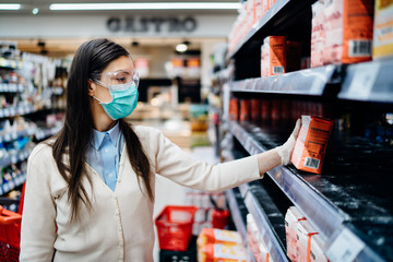 Woman wearing mask buying groceries/supplies in supermarket with sold out products.Food supplies flour shortage.Empty shelves due to novel coronavirus covid-19 outbreak panic buying and hoarding.