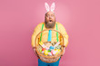 © deagreez - Portrait of his he nice amazed impressed funky glad bearded guy holding in hands giving you festal Easter craft basket bakery snack isolated over pink pastel color background
