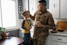 Soldier Father Put Camouflage Hat On Son In Kitchen