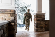 Female Soldier In Camouflage Returning Home On Snowy House Porch