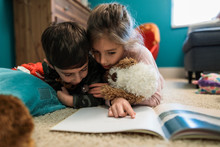Brother And Sister Reading Book On Bedroom Floor