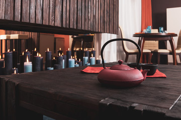 Tea pot with two cups on a wooden table with many candles burning on a background.