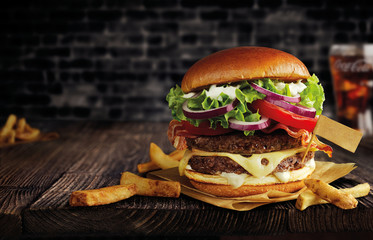 burger with double meat, cheese and french fries on a wooden table, with a flag, black brick wall behind