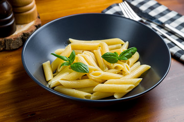 Poster - cooked Penne pasta on black plate with basil