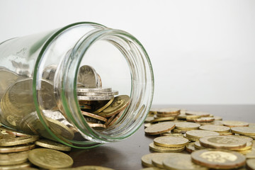 glass bottle surrounded by coins on wooden desk against white background. copy space. selective focus