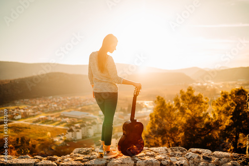 Fotografía Young guitarist holding an acoustic guitar and looking to sunset