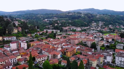 Aufkleber - drone flying above city with green landscape and mountains spring in italy