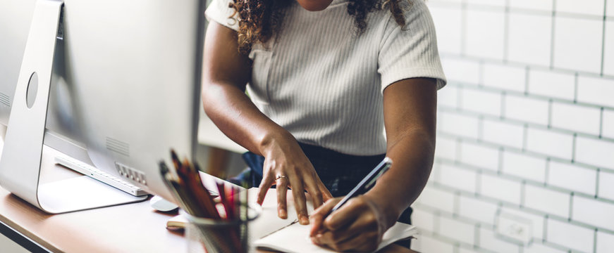 Portrait of african american black woman relaxing using technology of desktop computer while sitting on table.Young creative african girl working and write on book at home.work from home concept