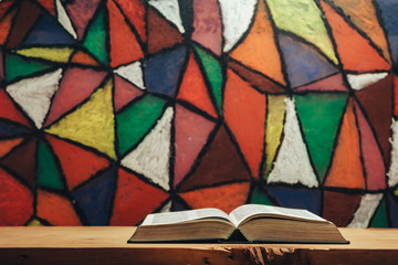 Wall Mural - Open Holy Bible on a red wooden table. Beautiful Stained-glass windows background behind. Religion concept.