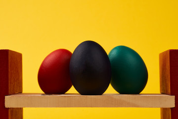 Colored black green blue red easter eggs on bright yellow background