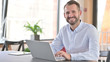 © stockbakers - Young Man with Laptop Smiling at Camera in Office