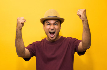 Happy young asian man celebrates with two hand in the air on yellow background.