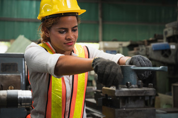 Female industrial worker working and checking machine in a large industrial factory with many equipment.