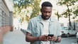© Sofiia - Handsome stylish african american young attractive man using phone walk on street smile sunlight sunset cellphone fashion internet face outside technology businessmen black young city mobile close up