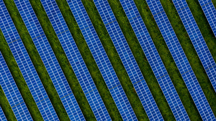 Aerial drone photo of a photovoltaic solar cell farm. Dark blue solar panels against a contrasting green grass field.