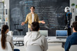 © pressmaster - Confident teacher of modern technology course talking to students at lesson