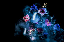 A Glass Perfume Bottle Shatters And Bright Spring Flowers And Clouds Of Blue And Purple Vapor Burst Out Of It Against A Dark Background