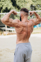 Handsome bearded bodybuilder man with perfect muscular body posing outdoors. Strong man with naked torso standing, looking away.
