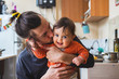 © Viktor Kochetkov - Hipster young father hug and kiss his baby infant boy holding on hands. At home on kitchen background. Lifestyle photo of family care and happiness concept. Middle class.