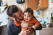 Hipster Young Father Hug And Kiss His Baby Infant Boy Holding On Hands. At Home On Kitchen Background. Lifestyle Photo Of Family Care And Happiness Concept. Middle Class. 