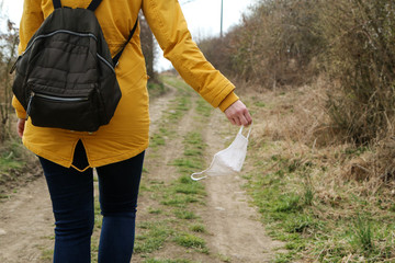 Woman is holding the textile home made face mask used for protection against viruses while walking in the nature. Symbol for protest against regulations or freedom after end of pandemic. 