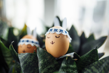 Two little easter eggs with a painted drawn rabbit faces and ears on it laying in the green flower bushes. Easter holidays decorations and preparations concept. Holy religious day.