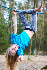 Wall Mural - Young child girl hanging on rope upside down on playground in park