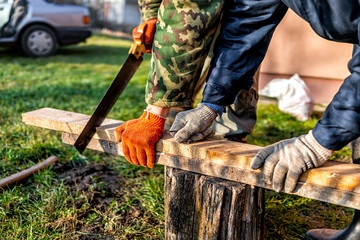 Two people men working in garden for post raised bed cold frame manual sawing wooden board in Ukraine dacha closeup