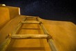 Low angle shot of a wooden ladder near the building under the dark sky full of stars