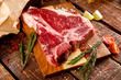 Raw T-bone Steak for grill or BBQ on cutting board over aged wooden background