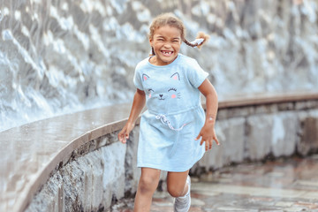 Happy beautiful girl running through the spray of water.