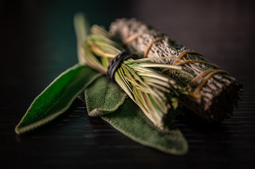 Closeup of Fresh & Dried Sage Native American Smudging Wiccan Bundles With Braided Sweet Grass Herbs On A Black Wooden Table Surface