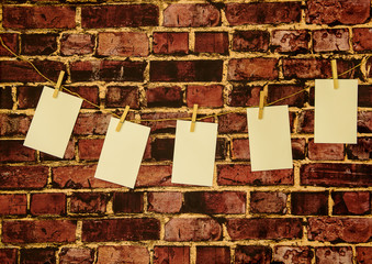 Background of photo sized papers on a rope with wooden pegs against a brick wall. Papers left blank for insertion of photos or illustrations.