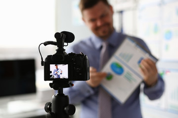 Male in suit and tie show stats graph pad making promo videoblog or photo in office camcorder to tripod portrait. Vlogger selfie solution or finance advisor management information professional concept