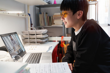 Asian kid learning from home on laptop in his bedroom during covid-19 quarantine