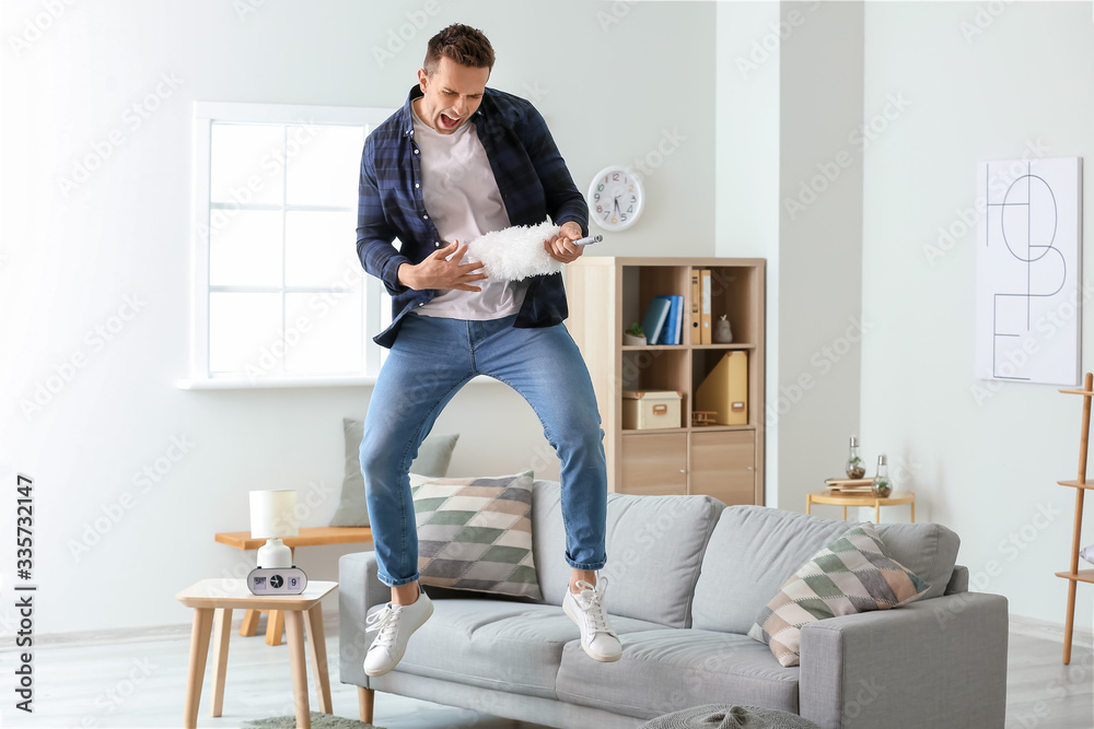 Cool young man dancing and singing while cleaning his flat
