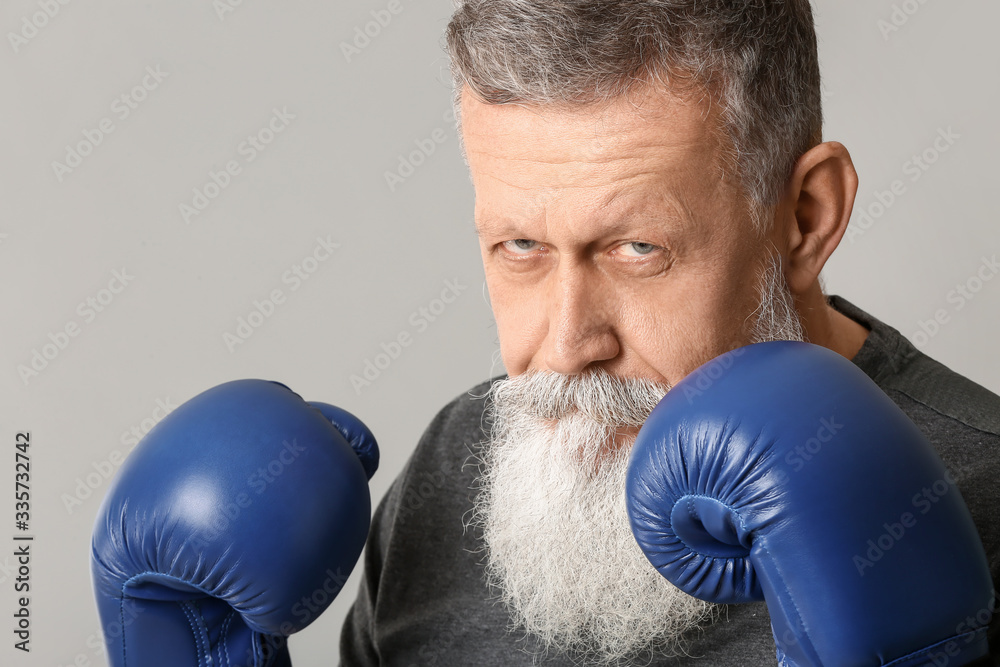 Sporty elderly male boxer on grey background