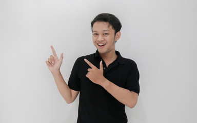 Happy and smile of young Asian man with hand point on empty space.  Indonesia Man wear black shirt Isolated grey background.