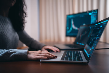 young female trader with laptop and screen looking at stock charts