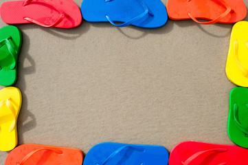 Wall Mural - Flip-flops in colorful orange, red, yellow, green, and blue forming a frame on textured sand beach