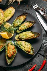 Wall Mural - delicious cooked mussels with sauce, lemon and garlic bread and butter on a black plate on the dark wooden background, top view, vertical