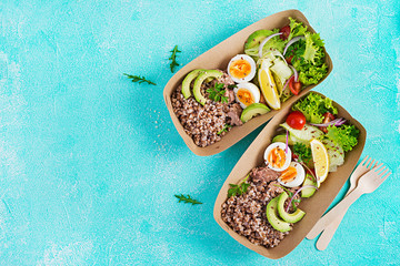 Healthy food delivery. Lunch- Buckwheat porridge, sliced tuna, boiled egg and fresh vegetable salad in zero waste containers  on blue background. Top view, flat lay