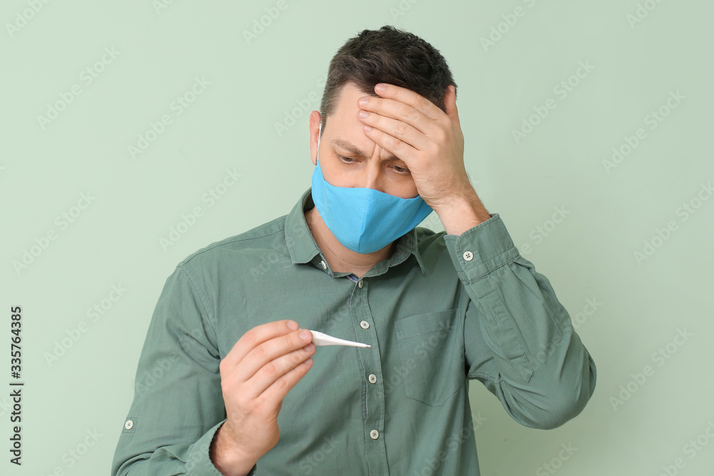 Man in protective medical mask and with thermometer on color background