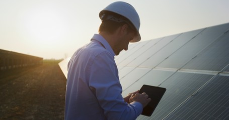 Wall Mural - an young engineer is checking with tablet an operation of sun and cleanliness on field of photovolta