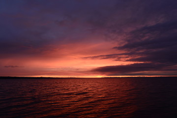 Wall Mural - Sun flare in the cloudy sky at sunset on the horizon over water lake