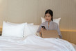© Pornchai - Young asian woman relaxing in the hotel and working with laptop on a bed, calling to cusotmer, Business trip, Working travel concept