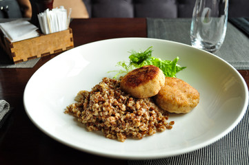 Chicken meatballs with buckwheat decorated with a green leaf on a white plate. 