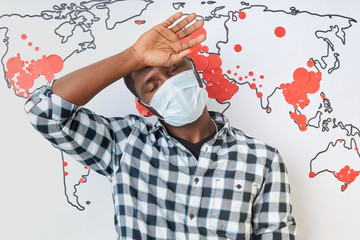 young african man suffering from high fever during coronavirus pandemic all over the world. man in medical mask stand in the background of world map. COVID-19 epidemic