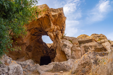 Rocky cave against the blue sky. The tunnel of limestone and wood. Rocky shore. Stony soil. The stones are beige and the sky is blue. Natural scenery